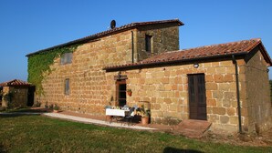 Un bâtiment en pierre avec un toit en tuiles, un petit porche avec une table et des chaises, et une porte.