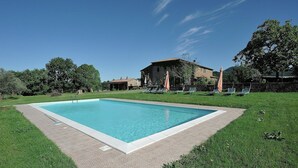 Une piscine rectangulaire dont le bord est recouvert de carreaux, entourée d’une pelouse et d’un mur en pierre.