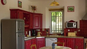 A kitchen with red cabinets, a refrigerator, a microwave, and a dining table with chairs.