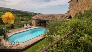 A stone building with a tiled roof, a swimming pool, and a garden with a yellow flower.