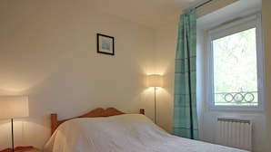 A bedroom with a bed, a nightstand, a lamp, a window with curtains, and a radiator.