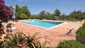 A rectangular swimming pool with a tiled deck, surrounded by lush greenery and a clear blue sky. - Algarve Casa with Pool (Loulé)