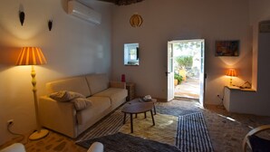 A cozy living room with a sofa, a coffee table, and a lamp. There is a door leading outside, and a painting on the wall. - Algarve Casa with Pool (Loulé)