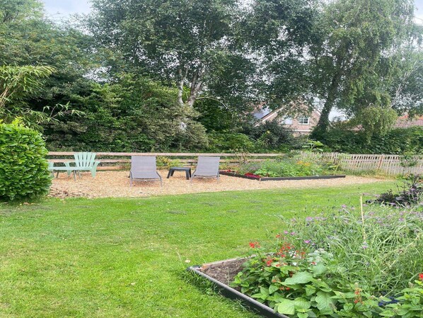 A garden with a wooden fence, two green chairs, and a variety of plants.