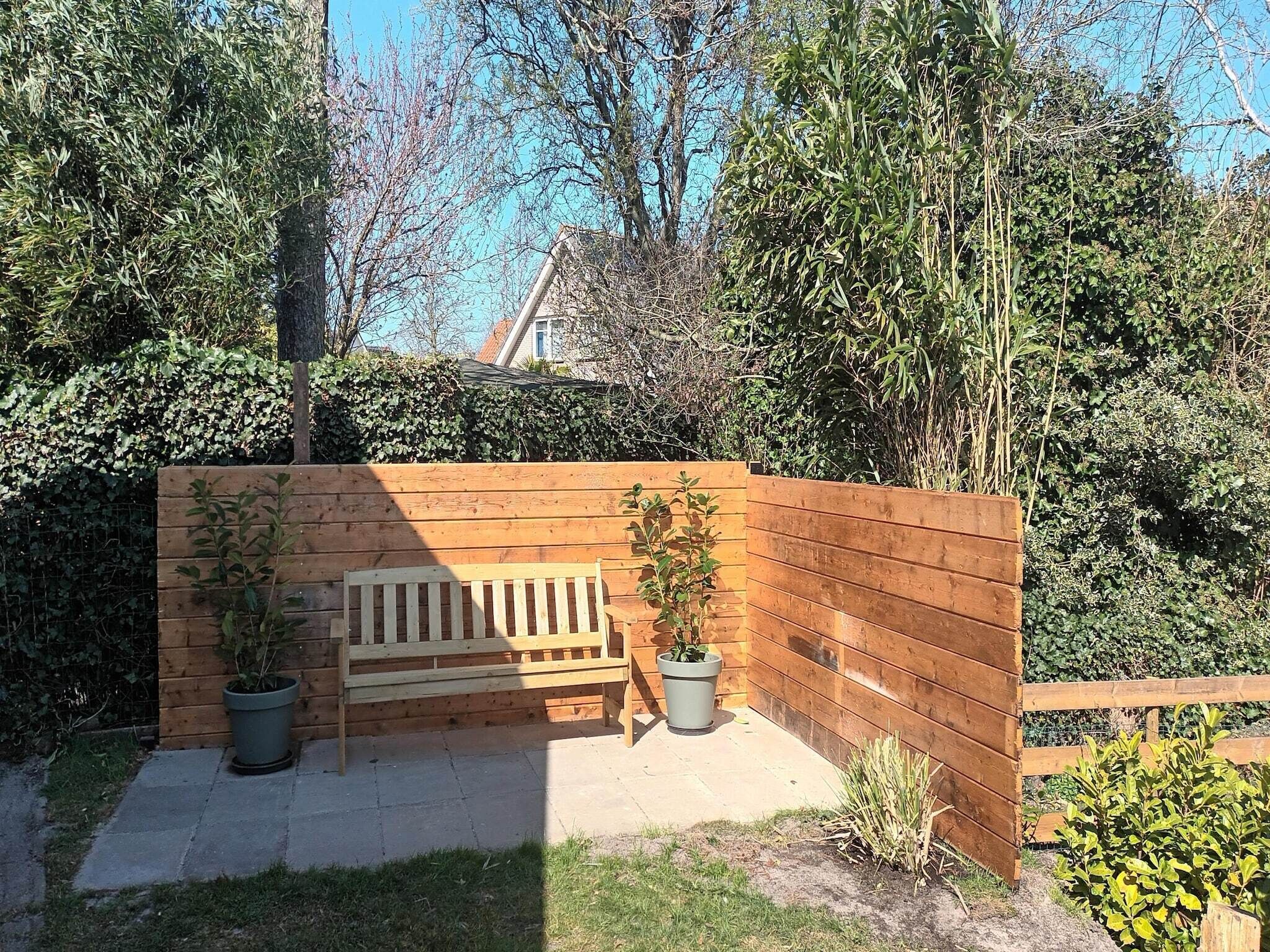 A wooden bench and potted plants in a garden area with a wooden fence and dense foliage in the background.