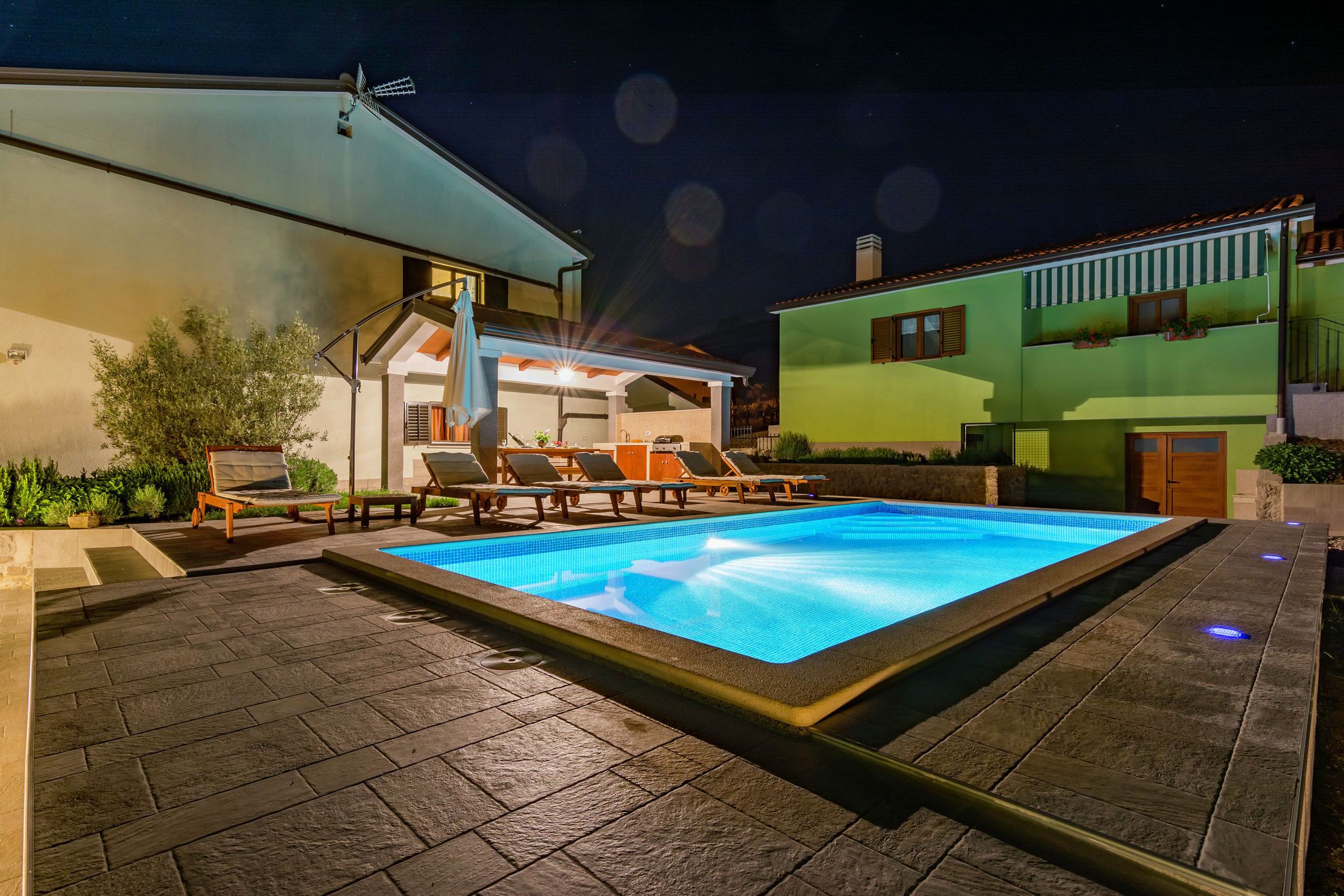 Une piscine avec des chaises longues, un patio couvert et une maison à la façade verdoyante.