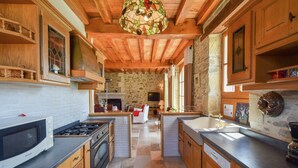 A spacious kitchen with wooden cabinets, a central island, and a stone wall. - Elegant Villa in Saint-Médard (St. Medard D'excideuil)