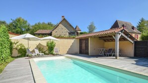 A swimming pool with lounge chairs and umbrellas, surrounded by stone buildings and a wooden deck. - Elegant Villa in Saint-Médard (St. Medard D'excideuil)