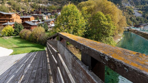 A wooden deck overlooking a river, with traditional wooden buildings and a forested hillside in the background. - Lake-view chalet in Tignes, close to ski area (Tignes)