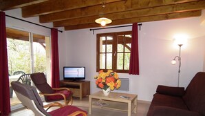 A living room with a wooden ceiling, a television, a coffee table with a vase of flowers, and two sofas. - Family Getaway in Dordogne (Gavaudun)
