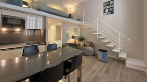 A modern apartment with a kitchen, dining area, and a staircase leading to an upper level.