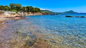Una playa con aguas transparentes y poco profundas, costa rocosa y una colina distante.