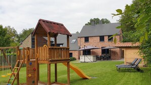 A wooden play structure with a slide and climbing wall, a brick house with a patio, and a lawn. - Elegant Villa in Bomal (Bomal-Sur-Ourthe)