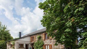 Een twee verdiepingen tellend stenen huis met een traditioneel ontwerp, met een combinatie van steen en vakwerk, een schoorsteen en een verharde oprit.
