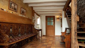 Een traditioneel interieur met een houten bank, een trap en een deur met een raam.