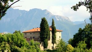 A stone building with a red roof, surrounded by lush greenery and mountains in the background. - Rustic Tuscan Cottage (Fivizzano)