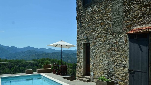A stone building with a pool, outdoor furniture, and a view of mountains. - Rustic Tuscan Cottage (Fivizzano)