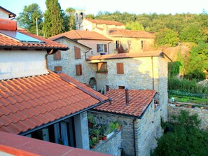 A stone building with a red-tiled roof, multiple windows, and a garden area with potted plants. - Rustic Tuscan Cottage (Fivizzano)