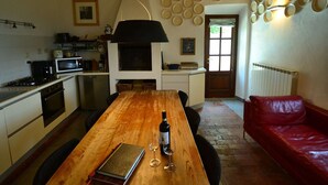 A cozy kitchen with a wooden table, a red leather couch, and a wall decorated with plates. - Rustic Tuscan Cottage (Fivizzano)