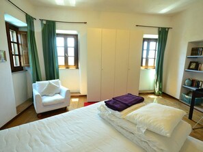 A bedroom with a bed, a white chair, a wardrobe, and a bookshelf. - Rustic Tuscan Cottage (Fivizzano)