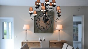 Une salle à manger avec une grande table, six chaises, deux lampes et une horloge au mur.
