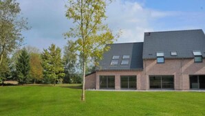 Une maison moderne à deux étages, dotée d’une façade en briques, de grandes fenêtres et d’un toit en pente.