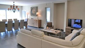 Un salon comprenant un canapé, une table à manger, des chaises, un téléviseur et un lustre.