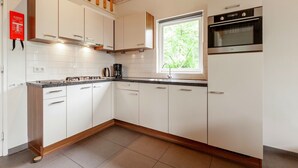 A modern kitchen with white cabinets, a built-in oven, and a window providing natural light. - Kempen Comfort with Sauna & Tub (Vessem)