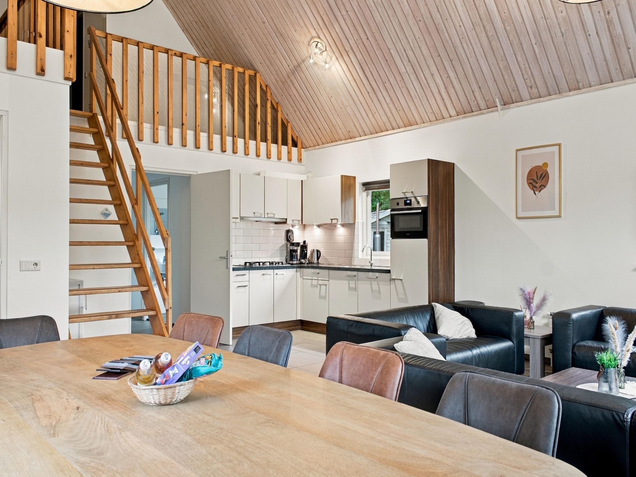A modern interior with a wooden staircase, a dining area with a wooden table, and a kitchen with white cabinets.