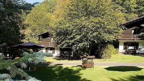 Una cabana amb un gran arbre al davant, un porxo cobert i un jardí ben cuidat.