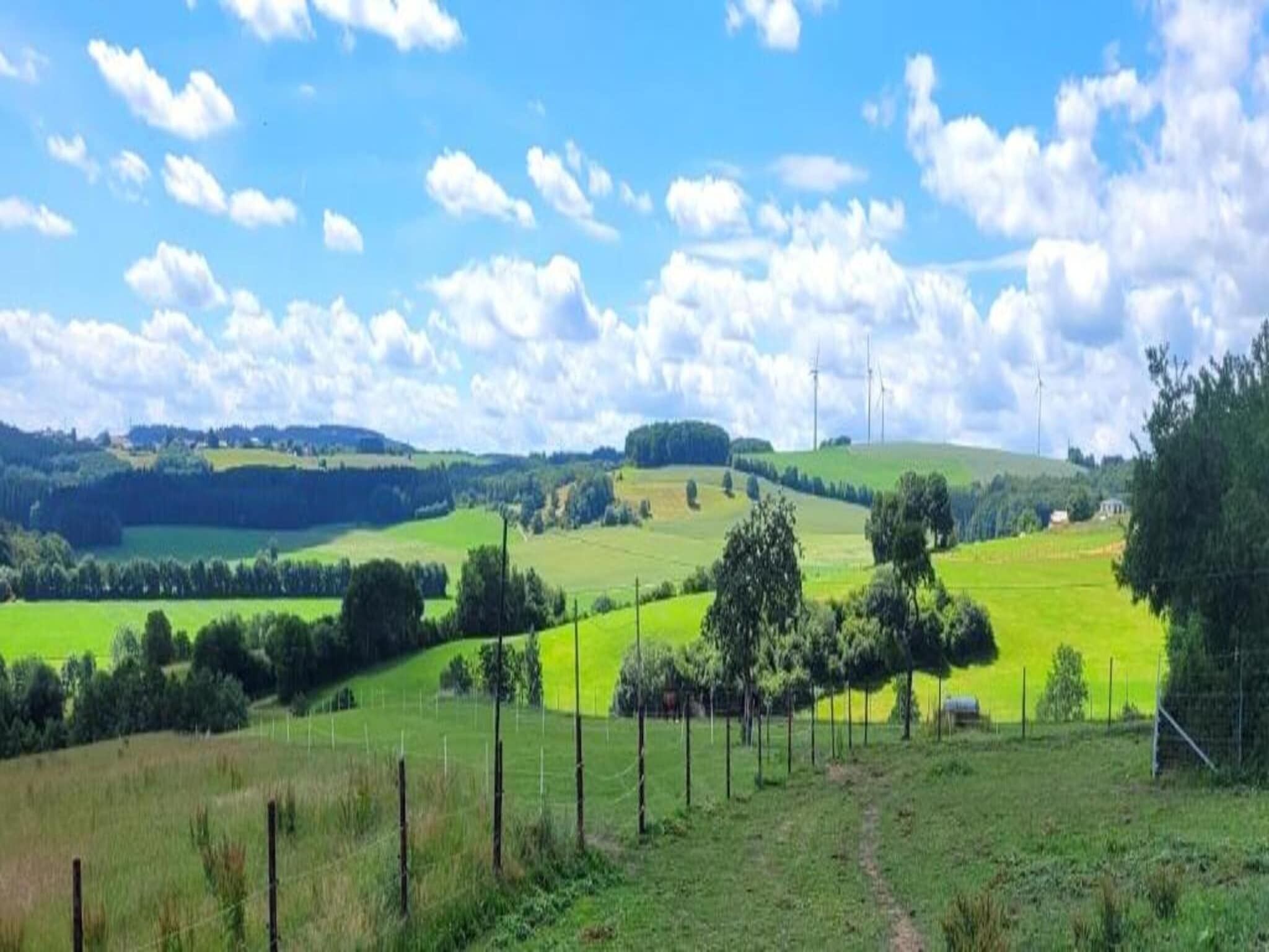 Ländliche Landschaft mit sanften Hügeln, grünen Feldern und einem klaren Himmel.
