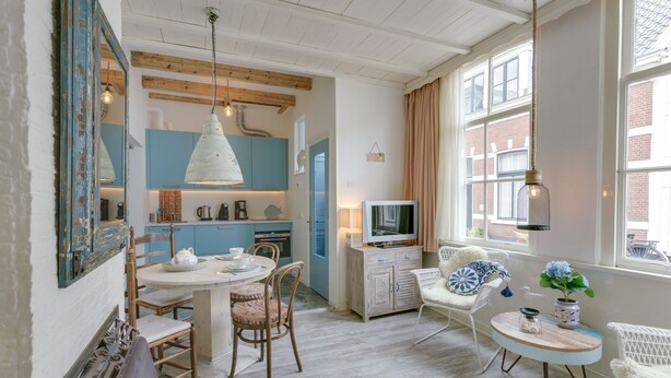 A cozy, well-lit room with a dining table, chairs, a television, and a window with curtains. - Picturesque fisherman's house near the beach (Scheveningen)