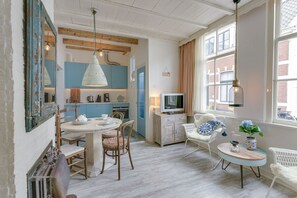 Une pièce chaleureuse et bien éclairée, avec une table à manger, des chaises, un téléviseur et une fenêtre avec des rideaux.