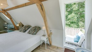 A bedroom with a sloped ceiling, a bed, a bedside table with a lamp, and a view of a balcony with outdoor furniture. - Picturesque fisherman's house near the beach (Scheveningen)