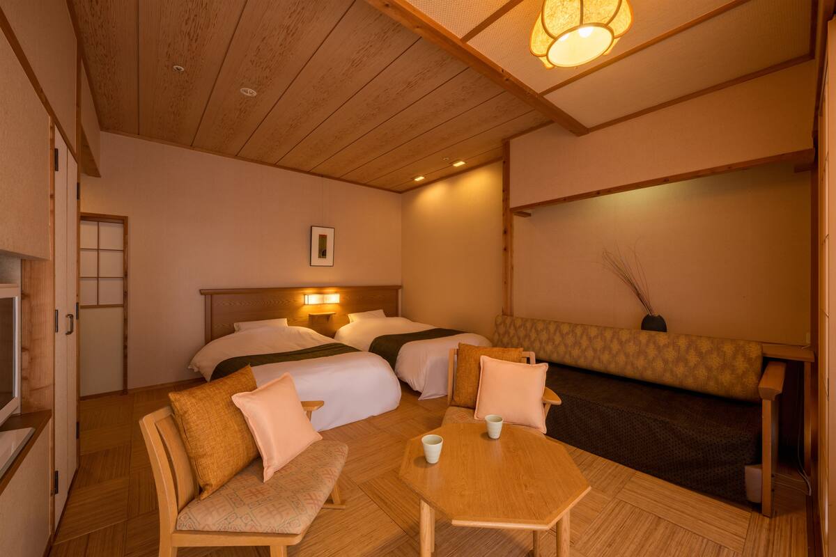 A hotel room with two beds, a sofa, a table, and a TV.