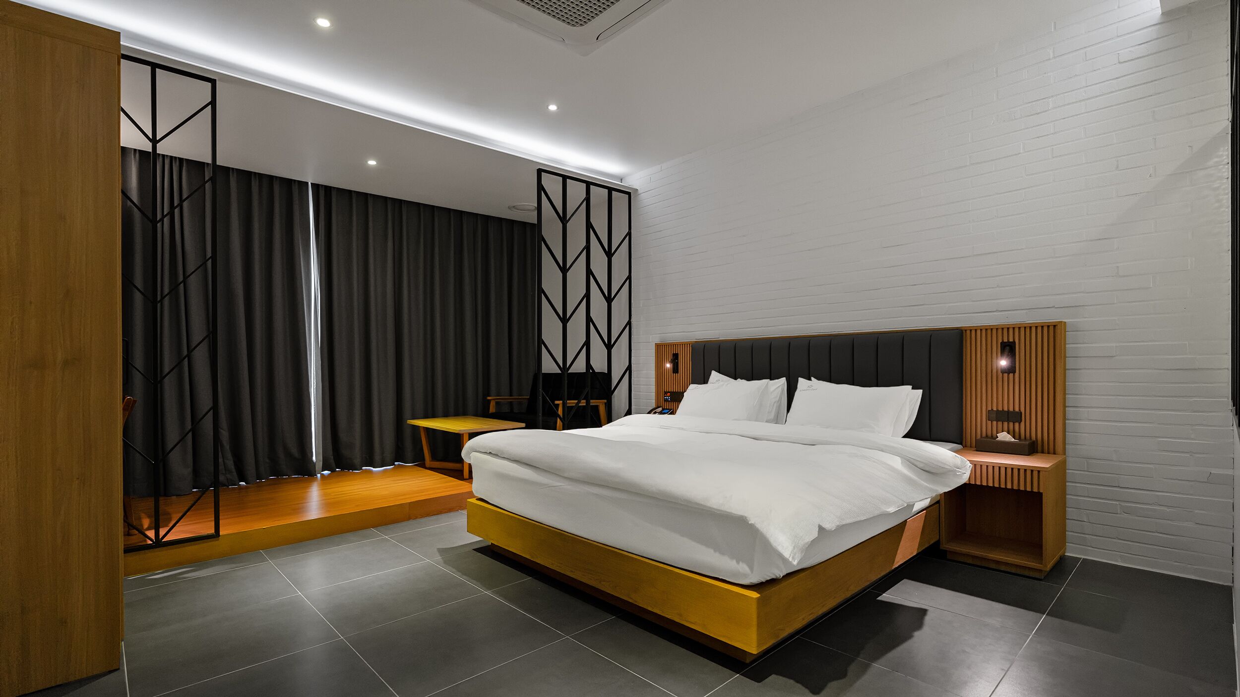A modern bedroom with a large bed, wooden headboard, and a nightstand with a lamp.
