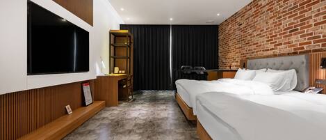 A modern hotel room with a large TV, a desk with a chair, a bed with white linens, and a brick wall.