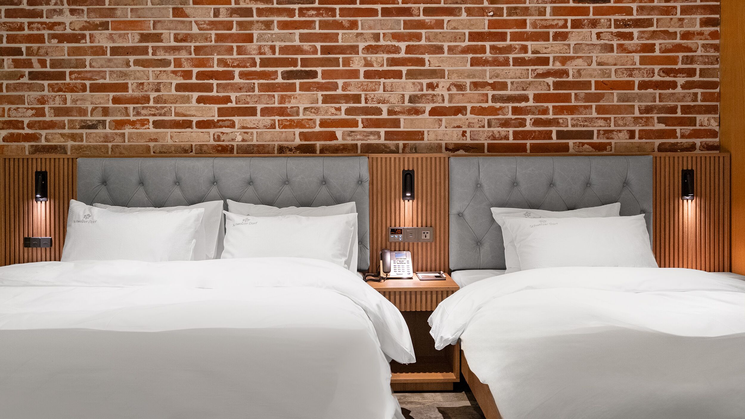 Una habitación de hotel con dos camas, un muro de ladrillo y un cabecero de madera.