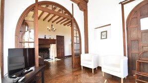 Un amplio salón con suelo de madera, chimenea, sofás blancos y un televisor sobre un mueble negro.
