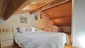 A cozy bedroom with a large bed, wooden ceiling beams, and a small desk.