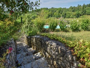 A stone wall with a rustic appearance, surrounded by lush greenery and flowering plants.