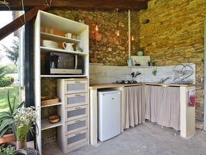 A compact kitchen with a stone wall, built-in shelves, a small refrigerator, and a window overlooking greenery.