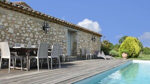 En bygning i sten med pool, udendørs møbler og en pergola.
