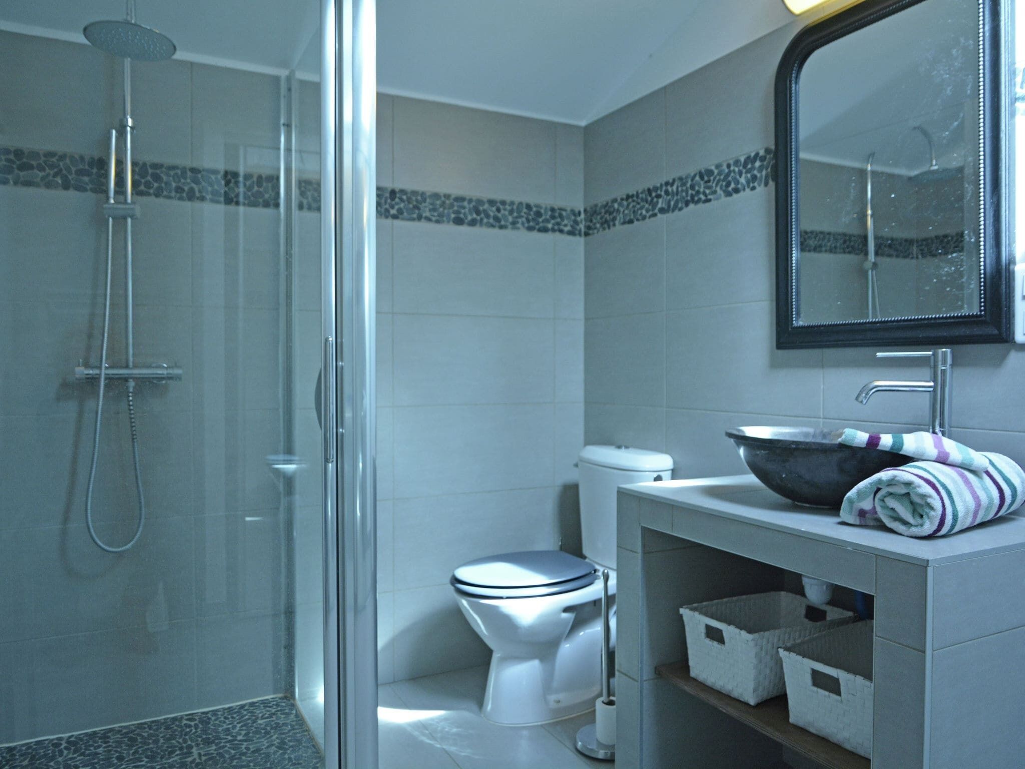 Une salle de bain moderne avec une douche à parois de verre, des toilettes blanches et un meuble-lavabo doté d’un miroir et d’un lavabo en forme de coupe.