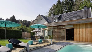 A modern house with a swimming pool, outdoor seating, and a wooden deck.