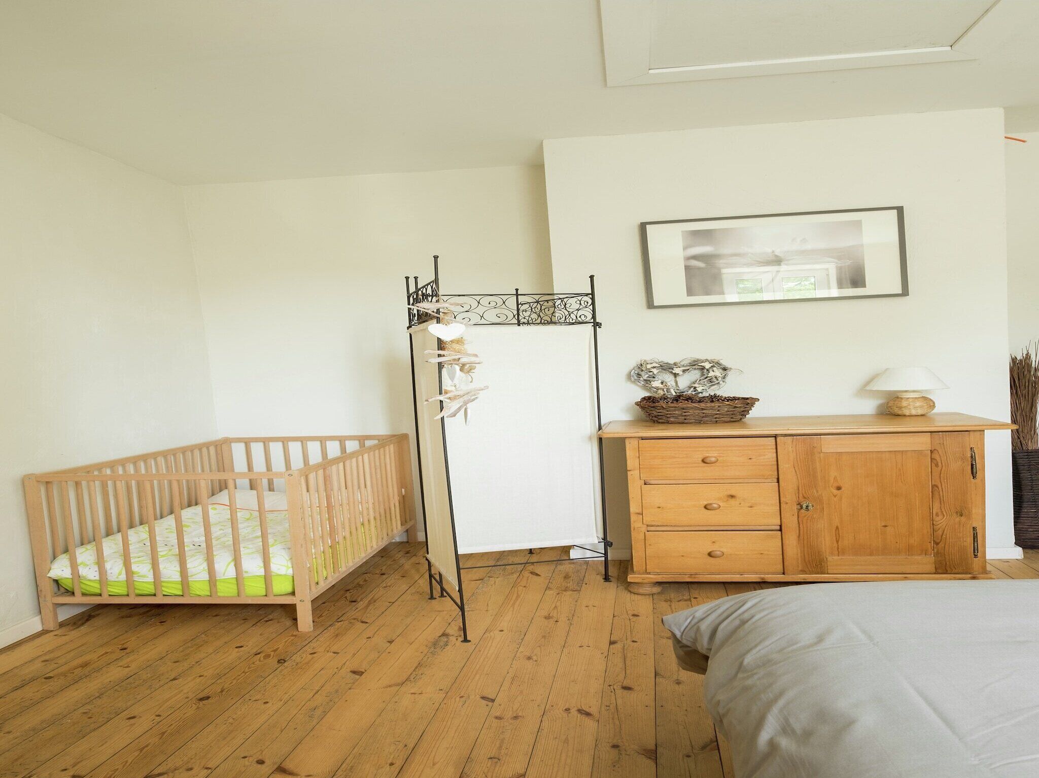 Une pièce avec un berceau en bois, une commode à tiroirs, un tableau encadré accroché au mur et une lampe posée sur la commode.