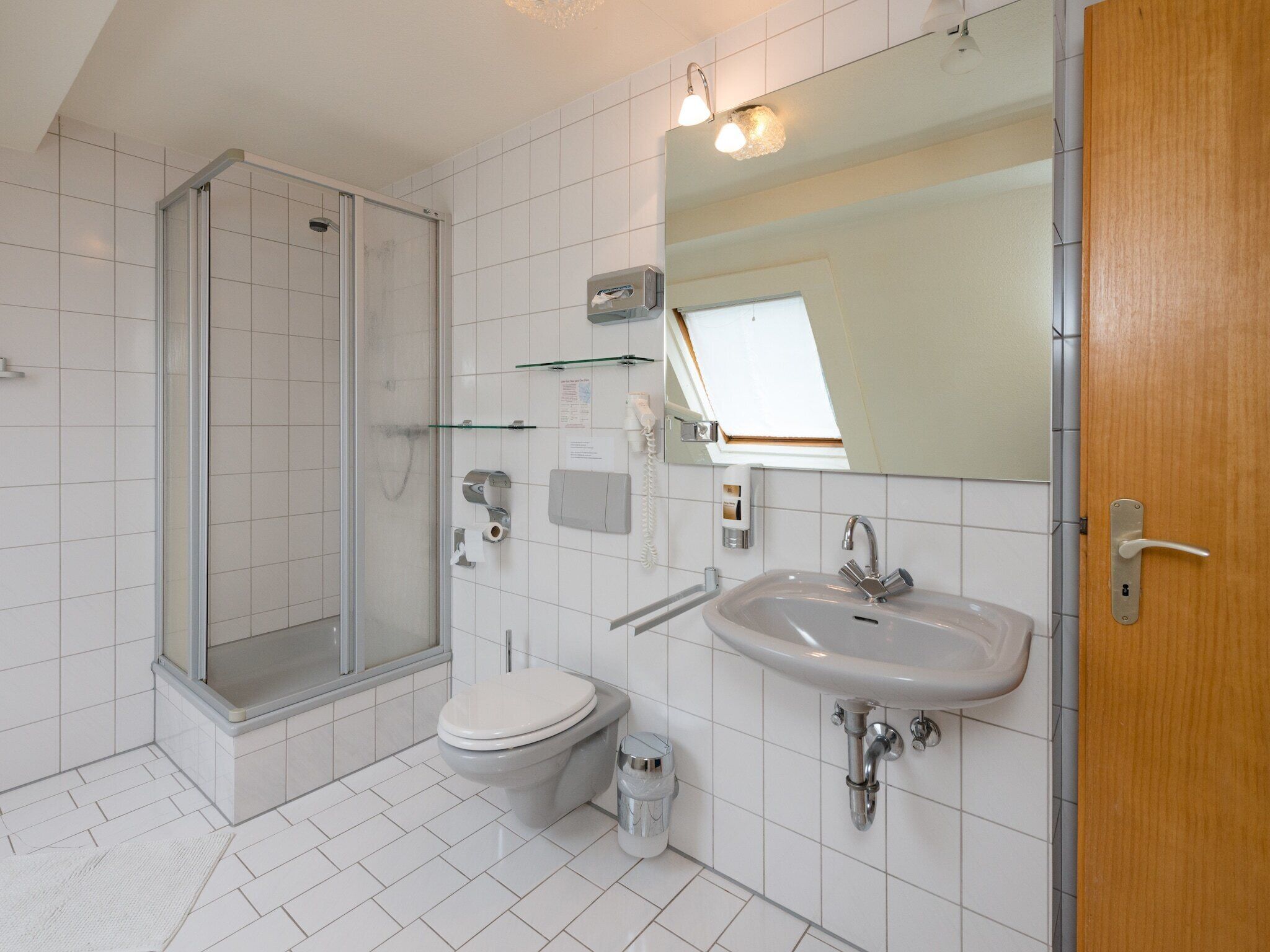 Et moderne badeværelse med bruser, toilet, håndvask og et stort spejl.