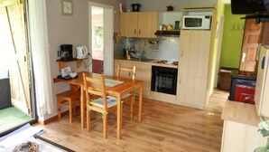 A compact kitchen with wooden cabinets, a microwave, and a stove. There is a dining table with chairs and a small breakfast bar. - The charm of a wooden chalet with a magnificent view, not far from Spa (Stoumont)