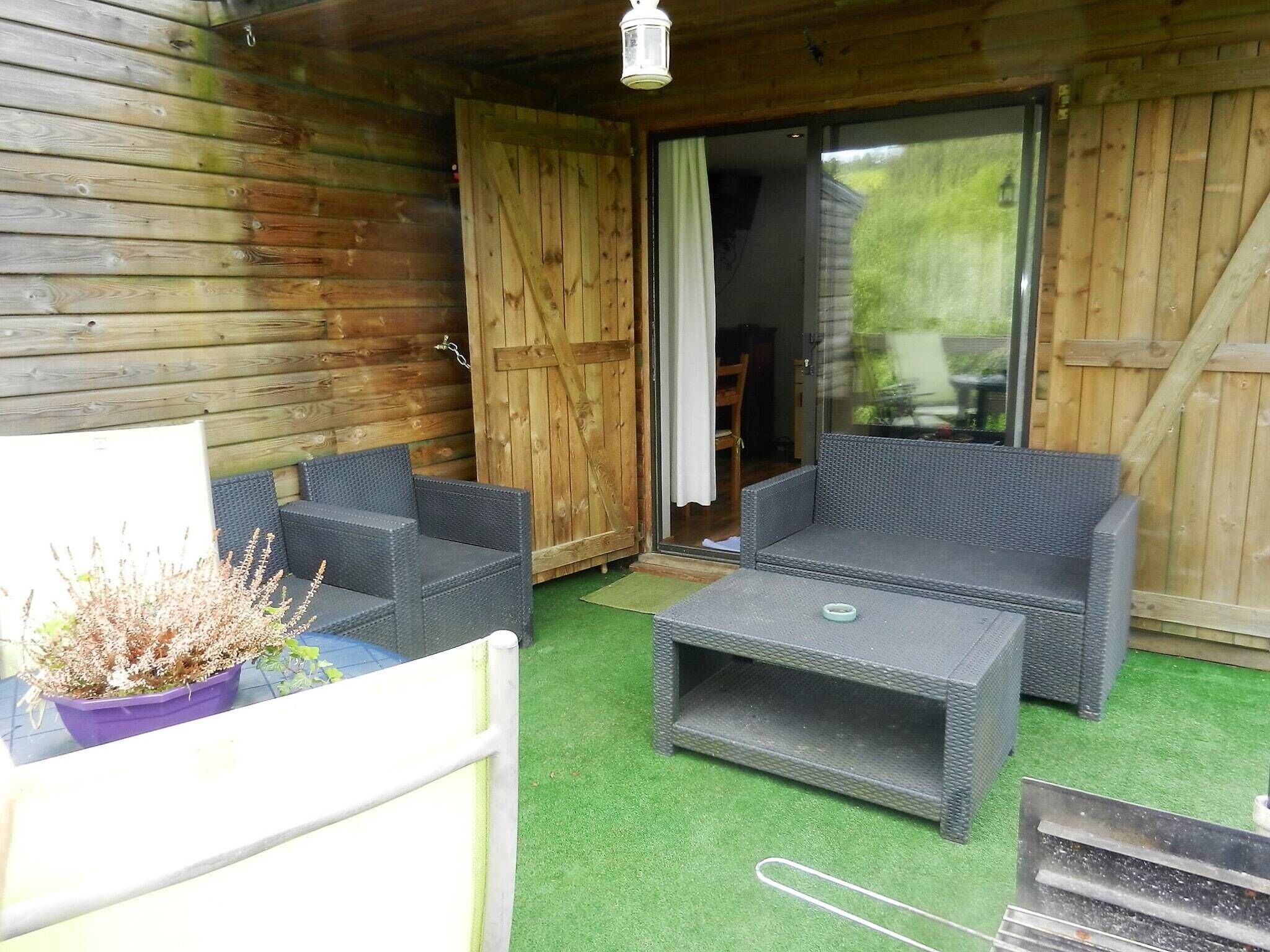 A wooden cabin with a sliding glass door leading to a patio area. Inside, there is a wicker sofa and a small table.
