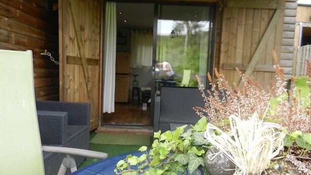 A wooden cabin with a patio area featuring outdoor furniture and potted plants. - The charm of a wooden chalet with a magnificent view, not far from Spa (Stoumont)